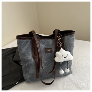 Detailed close-up of grey textured tote bag featuring a leather logo and fluffy cloud charm