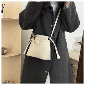 Detail of a creamy white drawstring bucket bag shown on a model in a grey tweed coat