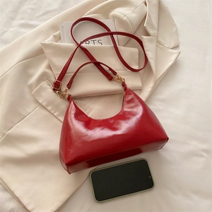 Glossy red half-moon shoulder bag with gold hardware shown with phone for scale
