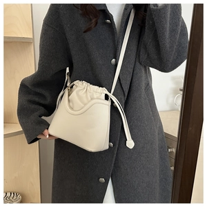 Detailed view of cream drawstring bucket bag worn over a dark grey tweed coat