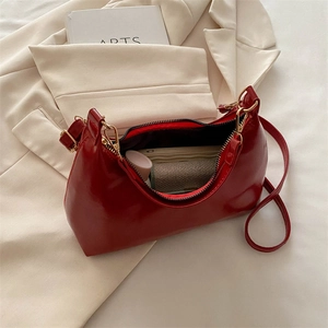 Glossy red faux leather hobo bag with gold zipper and spacious interior on beige blazer