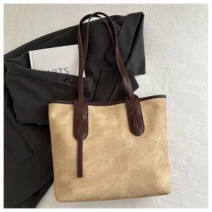 Top view of a tan canvas tote bag with dark brown straps over a grey blazer and props