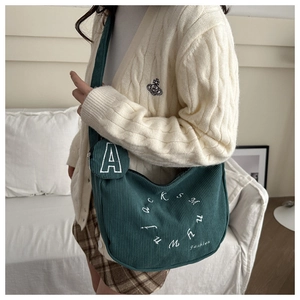 Close-up of dark green corduroy crossbody bag texture with white letter embroidery