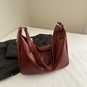 Glossy deep burgundy leather hobo bag with wide shoulder strap on white textured background