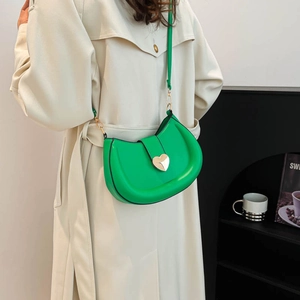 Bright green half-moon crossbody bag with gold heart clasp worn by model in trench coat