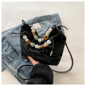 Detail of black pleated bucket bag featuring vibrant amber and emerald beaded handle