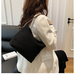 Détail d'un sac fourre-tout noir en daim avec bandoulière en cuir marron porté sur modèle