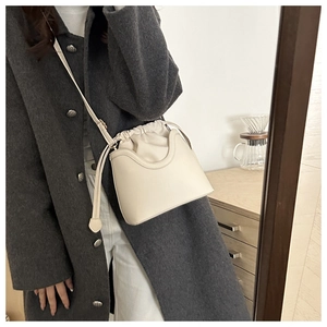 Cream white leather bucket bag with drawstring closure worn with a stylish grey coat