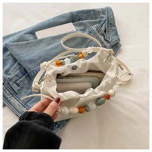Detail of white pleated cloud bag with colorful amber and emerald bead chain strap