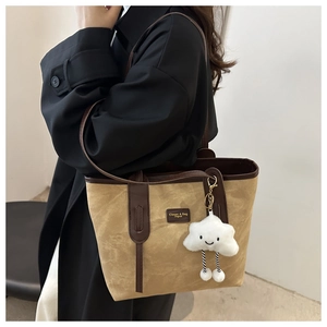 Detail of camel tote bag featuring contrast leather trim and a white cloud plush charm