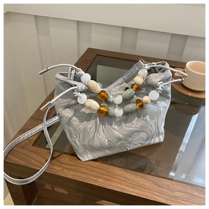 Chic silver marble bucket bag with colorful beaded handle on a wooden coffee table