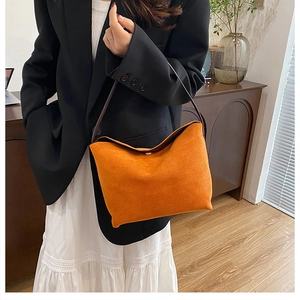 Détail du sac à bandoulière en daim orange vif avec sa fine lanière en cuir marron foncé