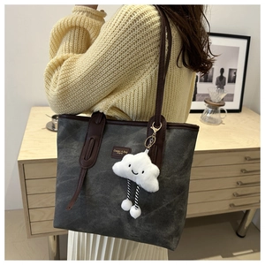 Detail of dark grey tote bag with leather straps and cloud charm worn by a model