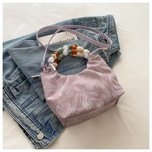 Detail of light purple bucket bag with marble pattern, colorful beads, and denim backdrop