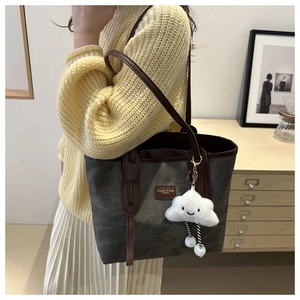 Detail of dark grey canvas tote bag featuring brown leather straps and a cloud charm