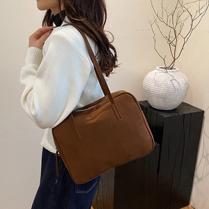 Detail of a large dark brown tote bag on a shoulder, showing texture and zip closure