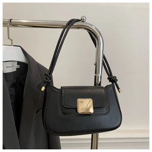 Detail of black leather underarm bag featuring a large gold buckle and knotted strap