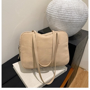 Detail view of beige matte suede tote bag on a book with long slim shoulder straps