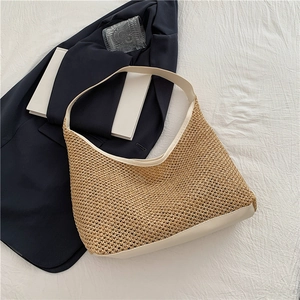 Detail of hand-woven straw hobo bag with white leather straps on a blue blazer background