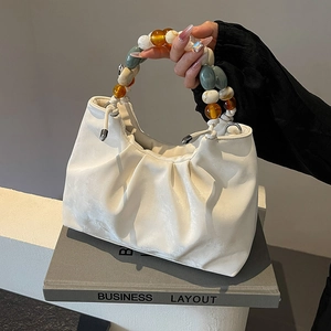 Minimalist white pleated cloud bucket bag with colorful beaded handle on a grey book
