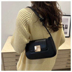 Detail of a black leather underarm bag with a large golden square metal buckle shown on a model