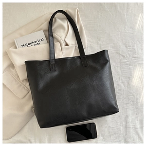 Detail of minimalist black PU leather tote bag shown with daily lifestyle accessories