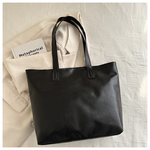 Close-up of black leather tote bag with pebble grain texture on white textured background