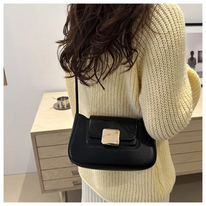 Close-up of minimalist black leather shoulder bag with decorative gold magnetic buckle