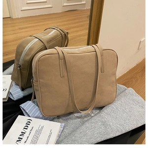 Detail of a large khaki suede shoulder bag with zipper closure in a minimalist setting
