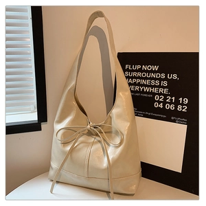 Detail of a large cream bow tote bag with soft glossy faux leather texture on display