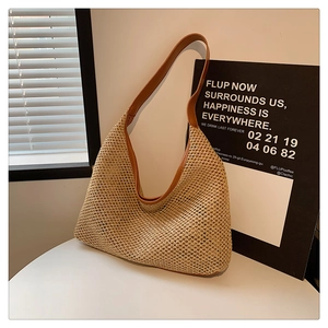 Detail of handwoven straw tote bag with brown leather shoulder strap on white table