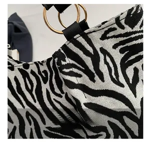Close-up of zebra pattern canvas bag with black leather handle and gold metal rings