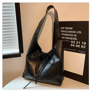 Detail of minimalist black hobo bag with ribbon bow and wide shoulder strap