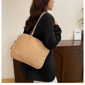 Minimalist beige leather shoulder bag worn by a model in a cozy, modern office setting