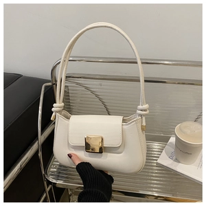 Detail of minimalist cream shoulder bag with gold buckle and unique strap knot design