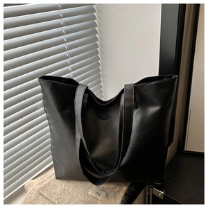 Detail view of large minimalist black tote bag with flat straps and smooth leather texture