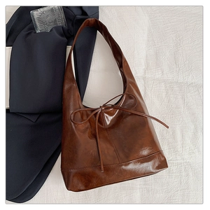 Detail of a deep brown hobo bag featuring wax leather texture and a bow ornament