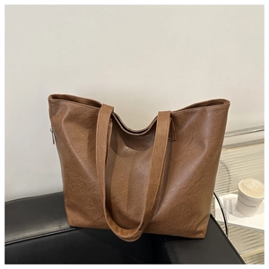 Close-up of retro brown pebbled leather tote bag with long straps on a black sofa