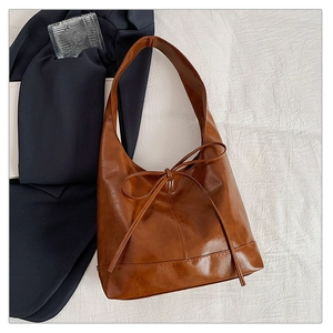 Detail of a brown glossy leather hobo bag featuring a slim bow tie decoration on a white fabric