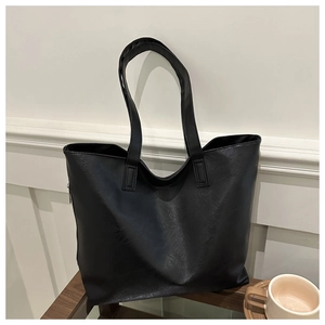 Close-up of black PU leather tote bag with long handles on a stylish glass table