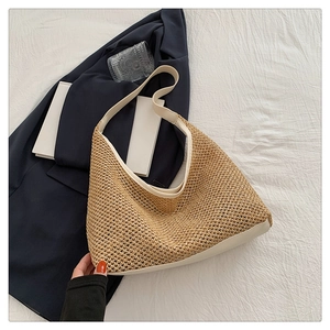 Close-up of a large straw tote bag with cream leather straps on a white textile surface