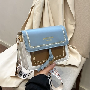 Chic blue and white color-block crossbody bag with wide floral woven strap in hand