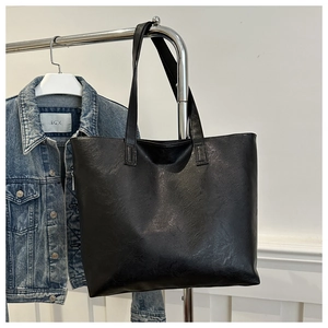 Detail of a large black tote bag in synthetic leather hung against a denim jacket