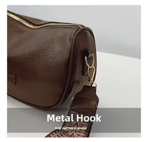 Close-up of brown leather cylinder bag with gold hardware and geometric patterned strap