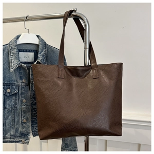 Detail of dark brown faux leather tote bag hanging next to a classic denim jacket