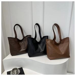 Three minimalist tote bags in brown, black, and caramel displayed on a white step