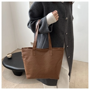 Detail of a brown textured tote bag with top zipper and slim shoulder straps on a model