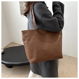 Detail of a brown tote bag with vintage pleated texture and shoulder strap on a model