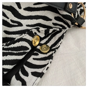 Macro shot of zebra pattern knit bag showing gold magnetic buckle and metal hardware