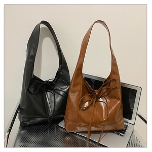 Detail of black and brown tote bags with decorative bows next to a laptop